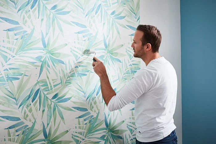 Person bringt Tapete mit Blättern an